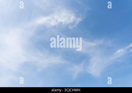 A serene view of a clear blue sky with scattered white clouds, offering a peaceful and calm ambiance. The clouds gently float across, creating a pictu Stock Photo
