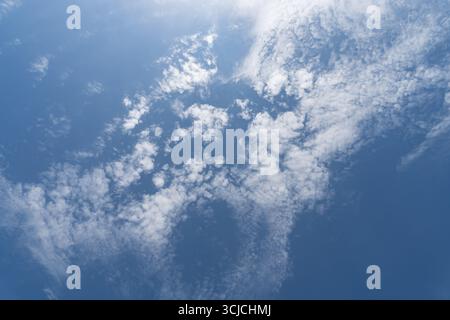 Image capturing a serene blue sky adorned with scattered white clouds viewed from below, creating a calming and expansive atmosphere. Perfect for back Stock Photo