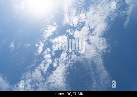 Bright sky with the sun shining through scattered white clouds, creating a serene atmosphere. The view from below captures the essence of a clear, sun Stock Photo