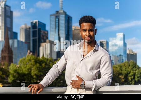 A confident mixed race businessman stands against Melbourne's iconic skyline, showcasing a modern, urban lifestyle. The image captures the essence of Stock Photo