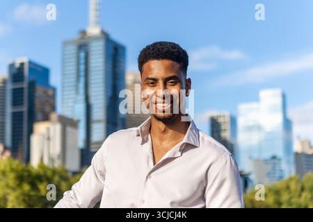 A young mixed race professional in a white shirt smiles confidently against Melbourne's stunning skyline. The urban backdrop captures the city's vibra Stock Photo