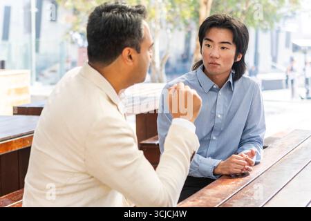 Two professional men having a focused conversation outdoors in Melbourne. The urban background and their attire suggest a business setting, highlighti Stock Photo