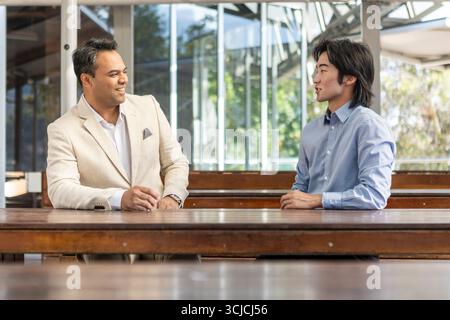 Two professional men engaged in conversation at an outdoor wooden table in Melbourne. A casual yet professional meeting scene ideal for business, netw Stock Photo