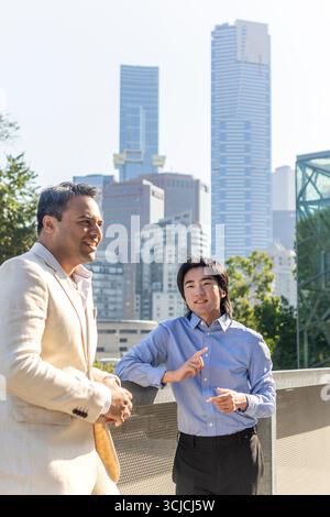 Two professional men engage in conversation outdoors with the Melbourne skyline in the background, highlighting urban business life and collaborative Stock Photo