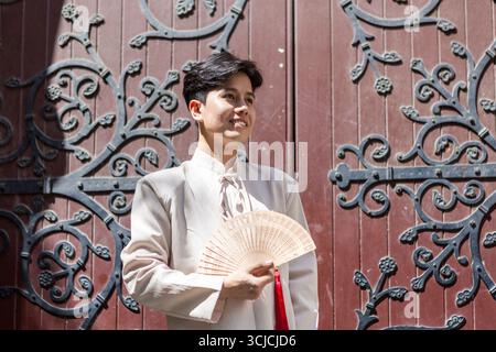 A Vietnamese man wearing traditional attire smiles while holding a fan in front of beautifully ornate historic doors in Melbourne. The scene blends cu Stock Photo