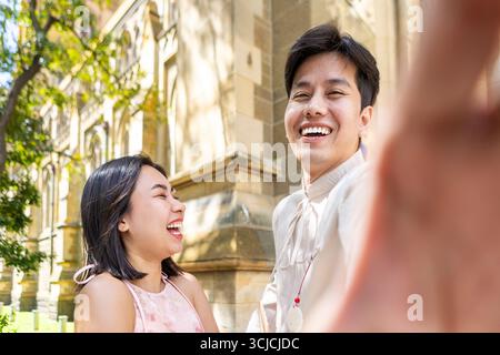 A smiling Vietnamese couple smiles brightly while taking a selfie in Melbourne. They wear traditional attire, blending cultural elegance with the urba Stock Photo