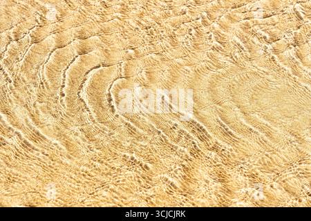 A detailed close-up of sea sand displaying intricate textures under a gentle ripple effect from the water. The image captures the serene beauty and fi Stock Photo