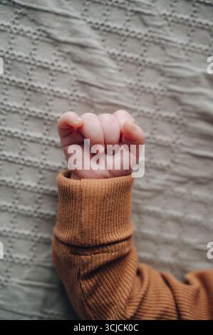 A close-up of a newborn's hand gently curled in a cozy, warm sleeve on a soft, textured fabric, symbolizing innocence and tender beginnings at one mon Stock Photo