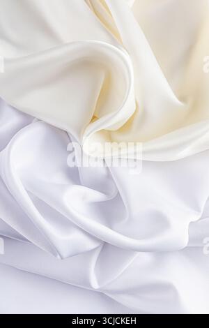 Luxurious satin fabric in ivory and white flows gracefully, creating a soft, elegant background. The silky texture and gentle folds add a touch of sop Stock Photo