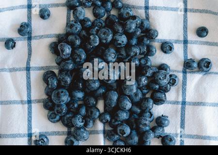 A clustered pile of fresh, ripe blueberries is spread over a blue and white checked cloth. The vibrant, deep blue tones highlight the berry's natural Stock Photo