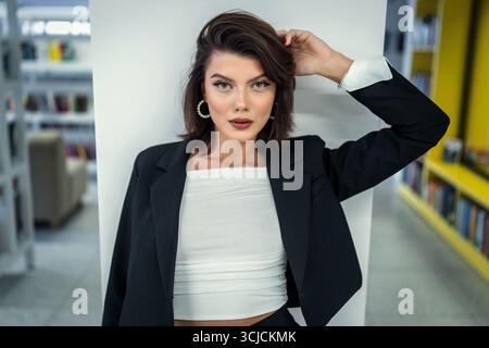 A sophisticated woman confidently poses indoors, wearing a stylish black suit. Her poised look and elegant attire create a professional and empowering Stock Photo
