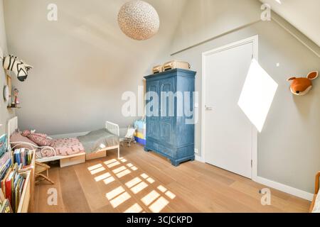 Bright children's bedroom with Scandinavian style, featuring a blue wardrobe, cozy bed, and playful decor. Sunlight streams in, highlighting the woode Stock Photo