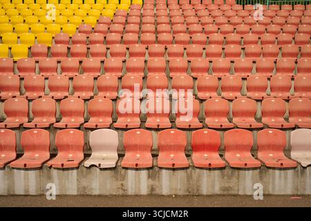 Rows of empty red and yellow stadium seats basking in the sunlight, ready to welcome spectators. The pattern creates a striking visual of anticipation Stock Photo