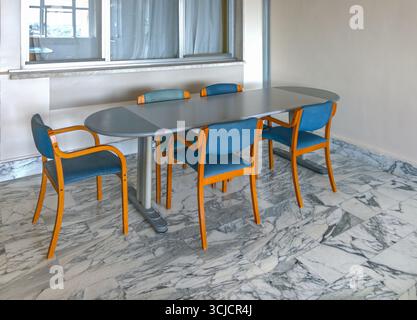 Oval table with wooden chairs upholstered in blue fabric on black-veined white marble flooring in the office meeting room Stock Photo