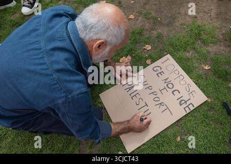 London, UK. 6th Sept, 2025.A person kneels on grass while writing a protest message on cardboard with a black marker. The sign reads OPPOSE GENOCIDE SUPPORT PALESTINE. Fallen leaves surround the individual, who wears a blue long-sleeve shirt and has grey hair. The scene captures a moment of quiet activism and personal expression in support of Palestine. Defend our Juries protest at the proscribing of Palestine Action with over 1000 people making a pledge to hold signs in defiance of Labour’s ban and showing support for the proscribed group. Penelope Barritt/Ģ����ý Live News Stock Photo