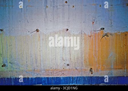 Wall texture in an abandoned factory, with white paint running over faded yellow and blue layers, photographed with direct flash on analog film. Stock Photo