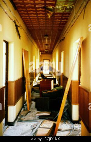 Abandoned factory corridor filled with scattered old furniture, peeling walls and signs of decay, captured in a raw atmospheric analog film aesthetic. Stock Photo