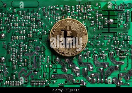 Golden coin with bitcoin symbol on a green printed circuit board with radio components on background, close up, top view Stock Photo