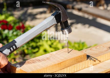 Worker using a hammer an metal nail into a wooden board, close up. Hand tool for working. Multifunction shockproof steel hammer and nail Stock Photo