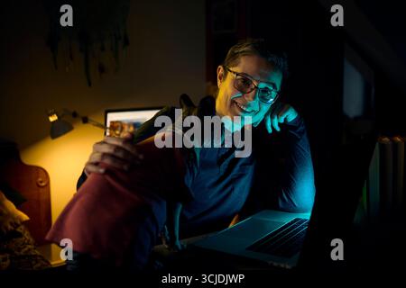 A professional woman works late on her laptop while cuddling her Canadian Sphynx cat in a cozy home office. The image shows a balance of remote work a Stock Photo