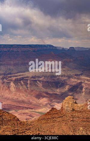 A dramatic, high-angle view of the Grand Canyon, showcasing its immense scale and multi-colored geological layers. The vast landscape features a spect Stock Photo