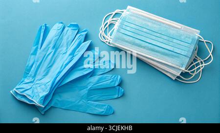 Disposable gloves and stack of medical masks made of non-woven material with white rubber bands on a blue background Stock Photo