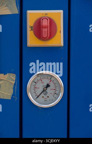 Close-up of industrial pressure gauge and red rotary switch placed on a blue metal panel background, representing machinery control equipment Stock Photo