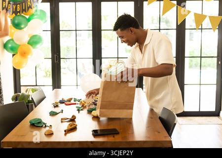 Man preparing birthday decorations on table at home, organizing festive items Stock Photo