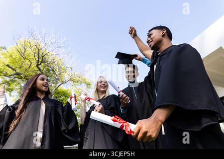 Celebrating graduates outdoors, holding diplomas, wearing caps and gowns, smiling joyfully Stock Photo