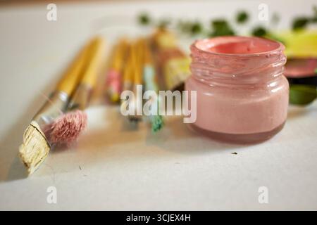 Creative arrangement of paintbrushes, watercolor palette, and pink paint jar on white background. Artistic workspace concept with bright colors and to Stock Photo
