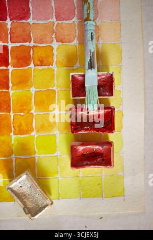 Close-up of watercolor paint swatches in warm tones with red paint pans and brush. Vibrant artistic composition perfect for creative projects, design Stock Photo