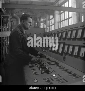 A Soviet operator at a monumental analog control panel in an industrial plant in Slavyansk, second half of the 1970s. This industrial portrait from the stagnation era captures a skilled worker in a moment of high concentration, managing a complex technological process, and symbolizes the industrial power and controlled creative energy of a peaceful Donbas Stock Photo