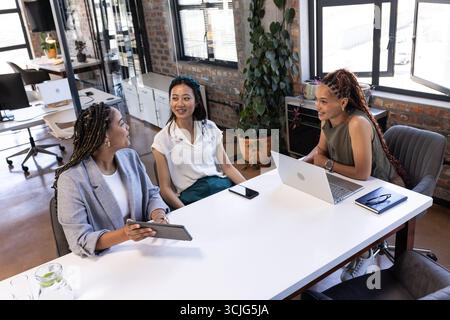 Businesswomen discussing project at office table with tablet and laptop Stock Photo