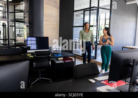 Colleagues walking through modern office, discussing work and holding coffee cups Stock Photo
