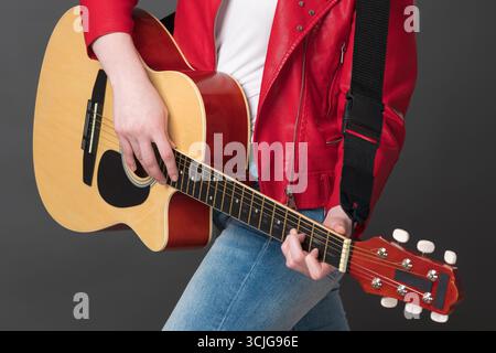 Unrecognizable woman guitarist playing acoustic guitar with concentration. Cropped view of midsection of stylish female rock musician dressed in red l Stock Photo