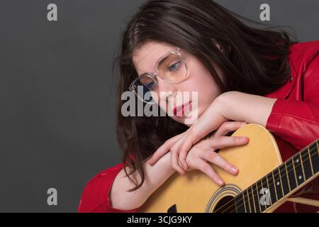 Female guitarist wearing glasses is resting thoughtfully. Woman musician has placed both hands on guitar and looking relaxed into distance Stock Photo