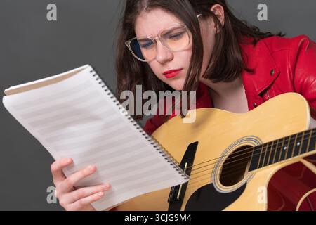Close-up view of female guitarist in glasses carefully studying sheet music as she is learning to play classical six string acoustic guitar Stock Photo