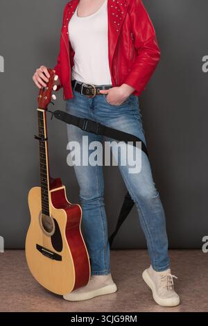 Front view of low section of female musician's body, with her classical guitar. Stylish musician is wearing red leather jacket and is holding guitar w Stock Photo