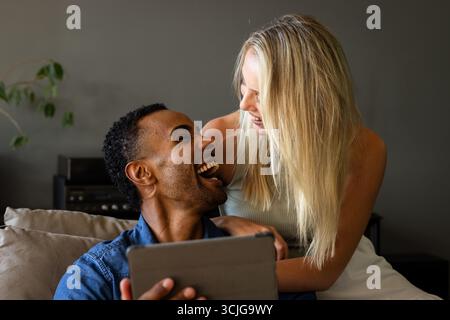 Couple laughing together while using tablet at home, enjoying relaxed moment Stock Photo