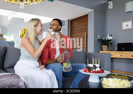 Couple celebrating at home, toasting with drinks and enjoying birthday cake Stock Photo