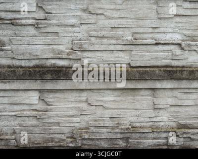 a fragment of an old, dilapidated, mossy concrete-stone fence with a rough, destroyed texture of the masonry, green traces of wet moss Stock Photo