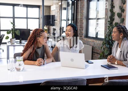Diverse businesswomen discussing project at office table with laptop and notebooks Stock Photo