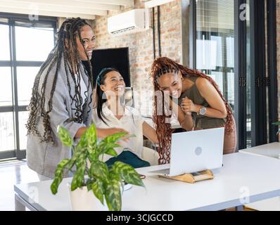 Colleagues celebrating success while video conferencing on laptop in modern office Stock Photo