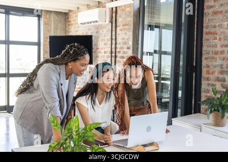 Collaborating in modern office, diverse women sharing ideas enthusiastically on laptop Stock Photo