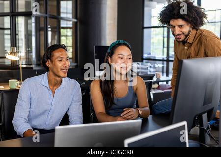 Collaborating in modern office, diverse team discussing project on computer screen Stock Photo