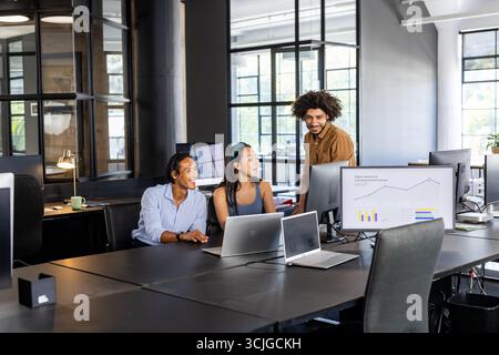 Collaborating in modern office, diverse team analyzing data on computer screens Stock Photo
