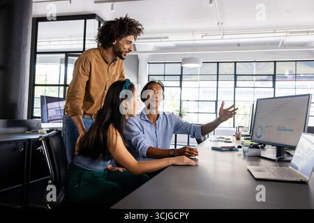 Diverse business team discussing project at office desk, analyzing data on computer Stock Photo