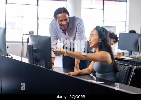 Colleagues collaborating at office desk, discussing project on computer screen Stock Photo