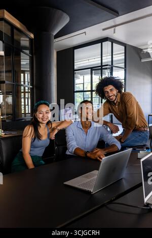 In office, diverse business team collaborating around laptop, smiling confidently Stock Photo