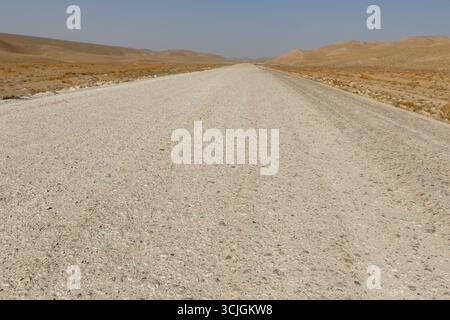 An empty and straight gravel road leads into the distance through a dry, barren desert valley in Kunduz Province, Afghanistan. Stock Photo